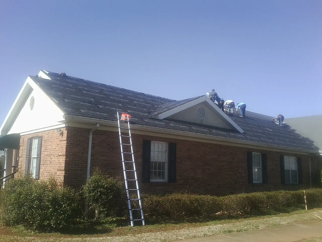 Crew tearing shingles off a brick ranch roof with a ladder set — Metal Roof Repair work by our crew in Descanso