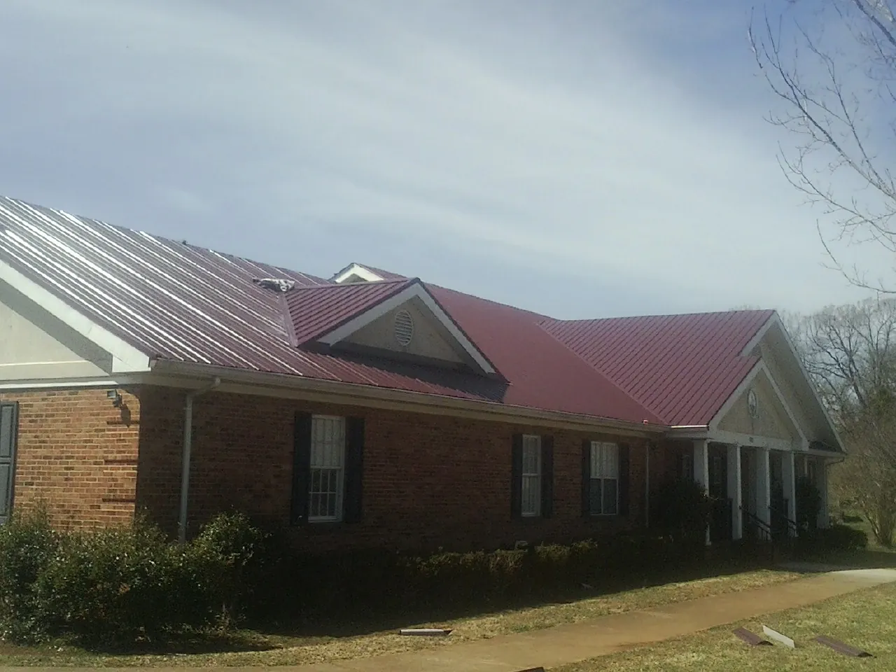 Red metal roof with gabled entries on a long brick building, from a Hail Damage Roof Repair job in Descanso