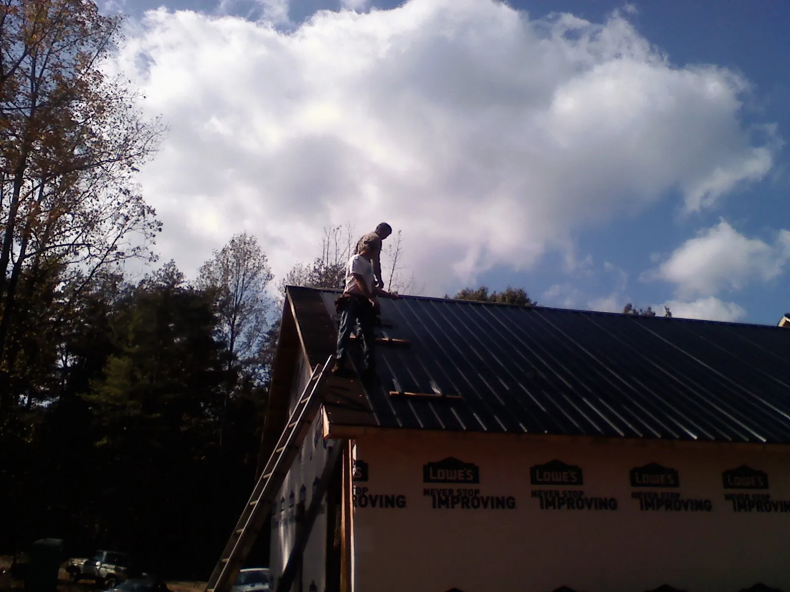 Roofer fastening dark metal panels high against a cloudy sky, from a Roof Inspection job in Descanso